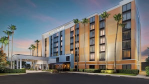 Un hotel moderno con un ingresso ben visibile, diversi piani e palme.
