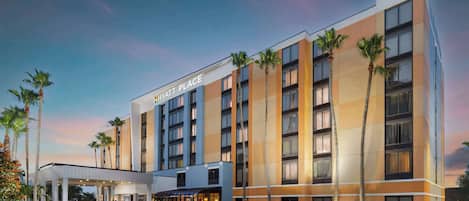 A modern hotel with a prominent entrance, multiple floors, and palm trees.