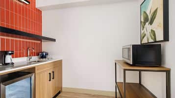 Una cocina compacta con un microondas sobre una mesita, un lavamanos y una cafetera.