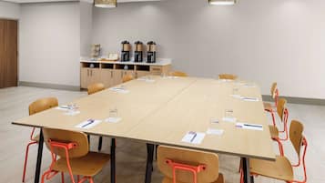A conference room with a long table, multiple chairs, coffee makers, and a cabinet with storage.