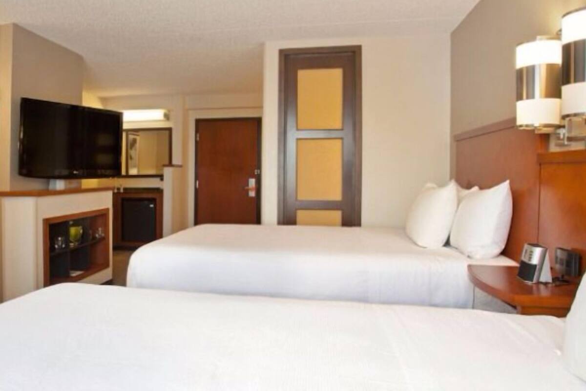 Een hotelkamer met twee bedden, een televisie, een deur en een nachtkastje met een lamp.