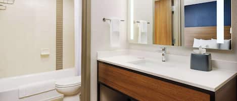 A modern bathroom with a bathtub, toilet, vanity with a mirror, and a shelf with towels.