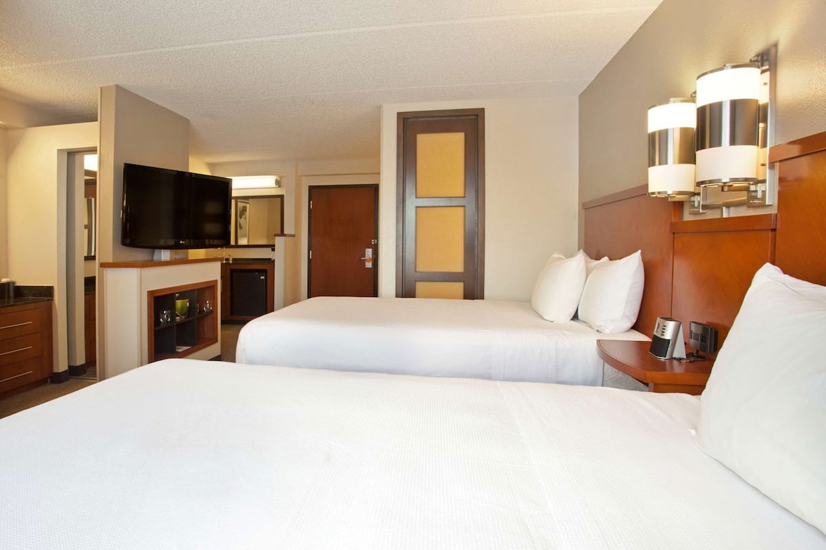 Hotelkamer met twee bedden, een televisie, een minibar en een houten hoofdeinde met wandlampen.