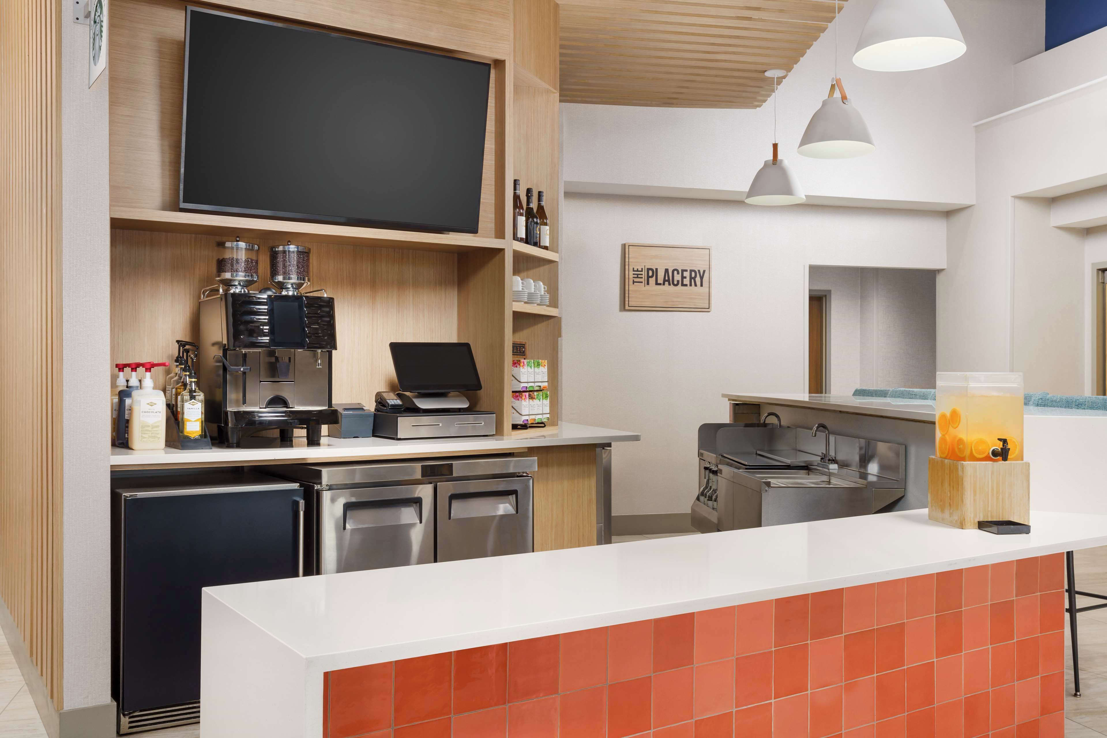 Una cocina moderna con televisión de pantalla plana, cafetera y un cartel que dice "The Plagery".