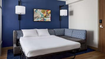 A modern hotel room with a large bed, a sofa, two wall-mounted lamps, and a colorful abstract painting on the wall.