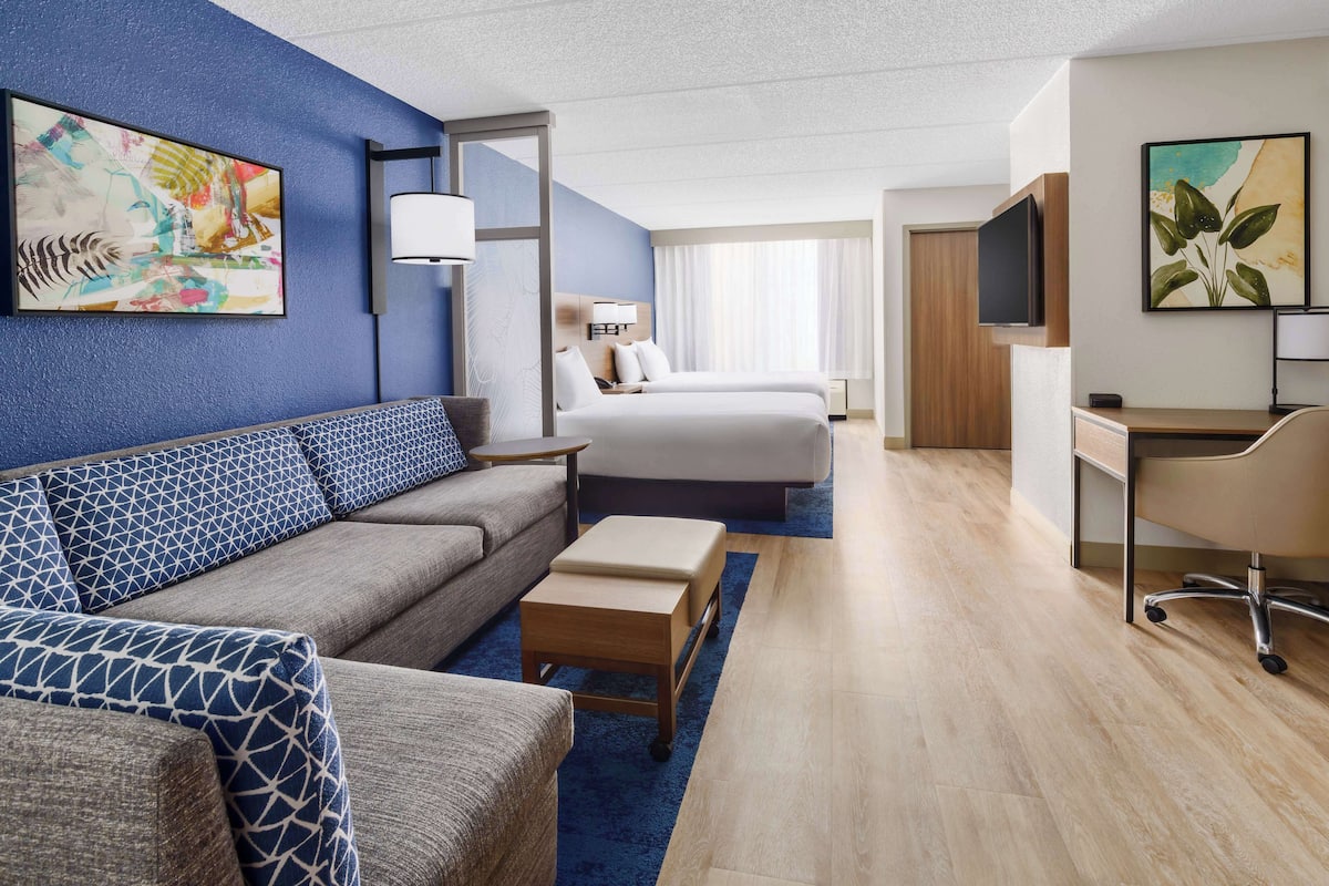 Hotelkamer met een blauwe accentmuur, een bank, een bed, een bureau en een televisie.