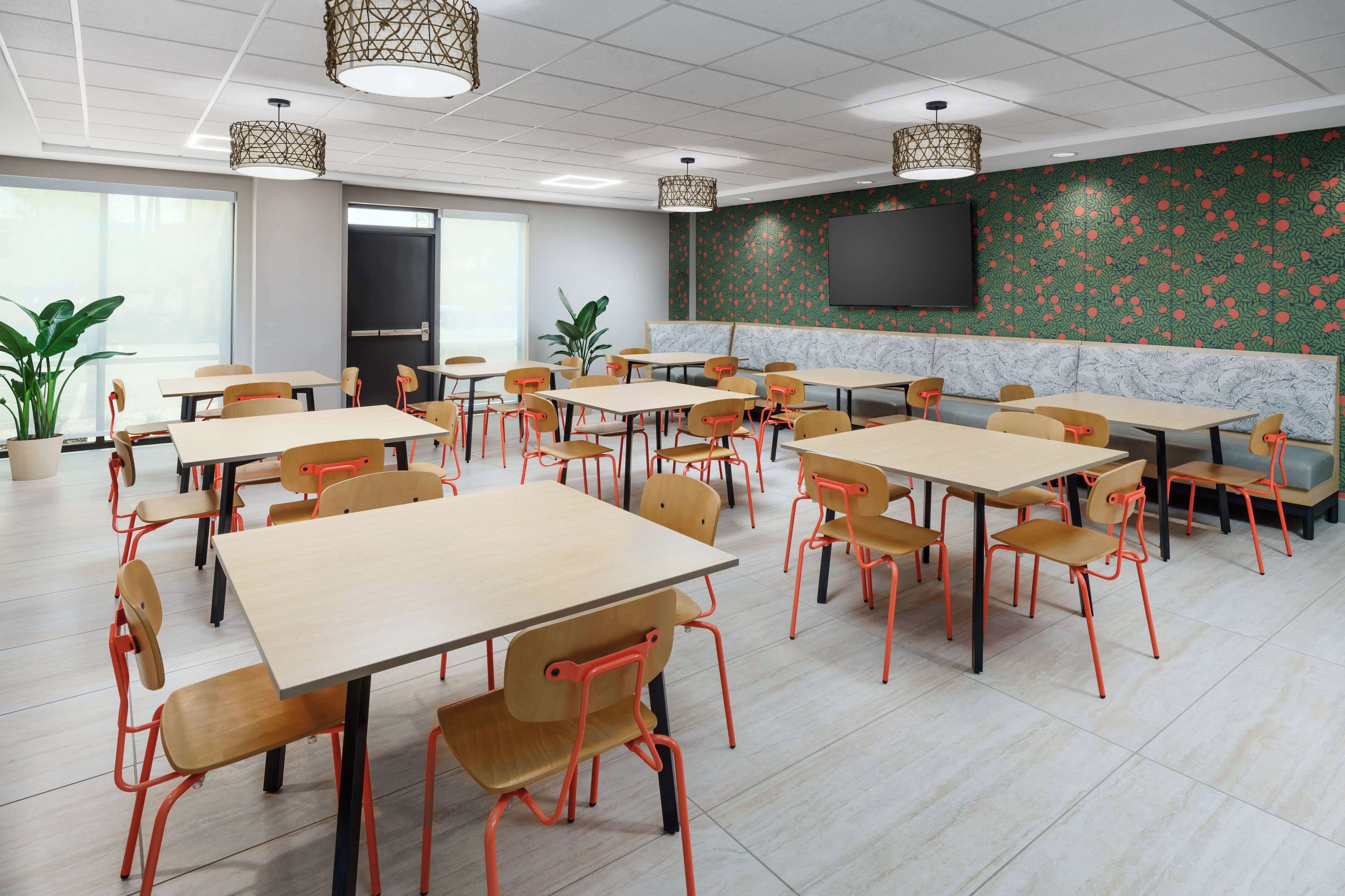 A conference room with multiple tables and chairs, a large screen, and a green patterned wall.