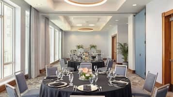 Un salón de conferencias con mesas redondas, sillas y un centro de mesa floral.