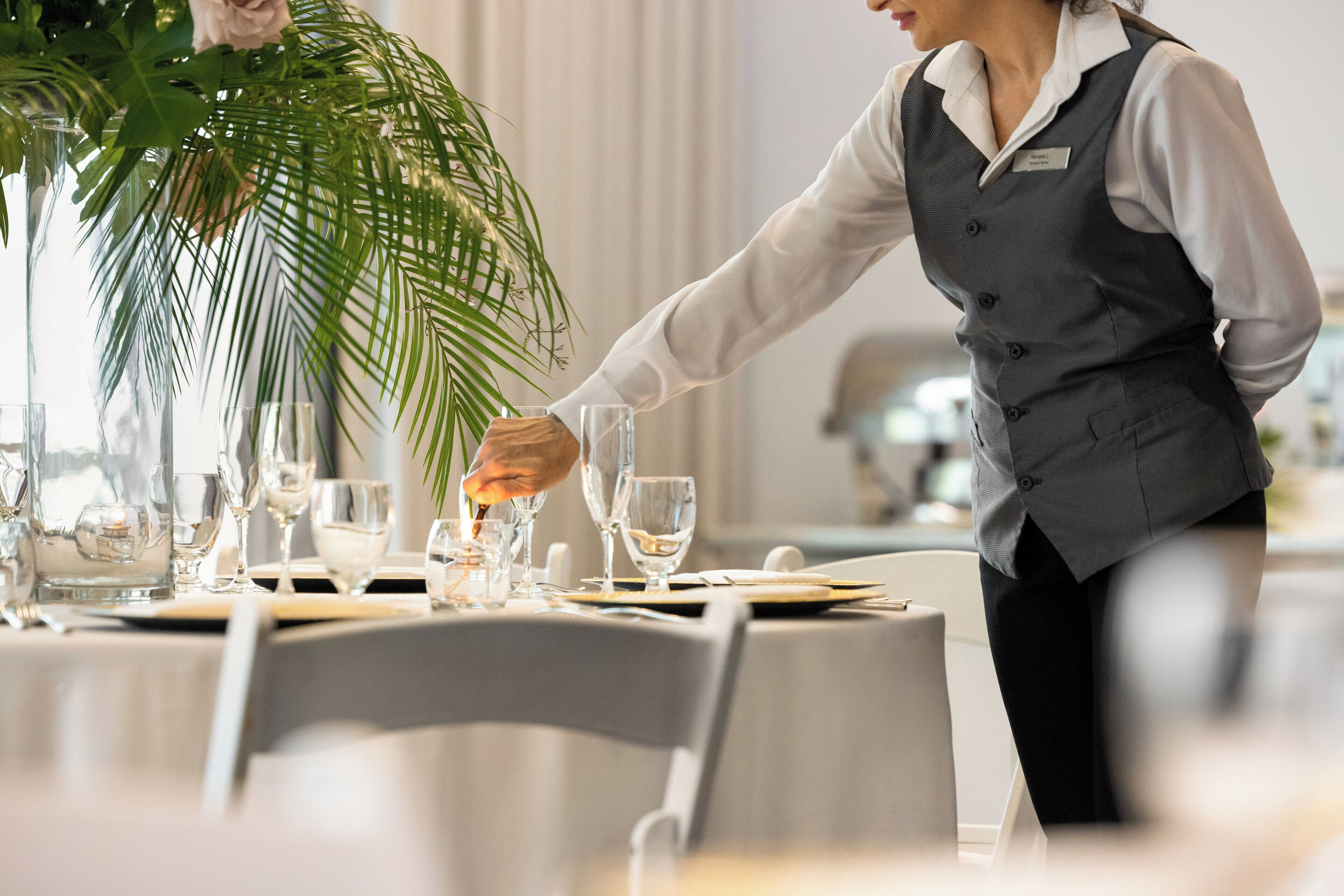 Una mesa de comedor bien dispuesta con una tarjeta de identificación, una planta en maceta y un camarero con uniforme.