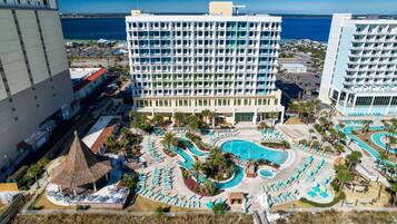 A hotel with multiple floors, a central swimming pool, and a beach area with sun loungers.