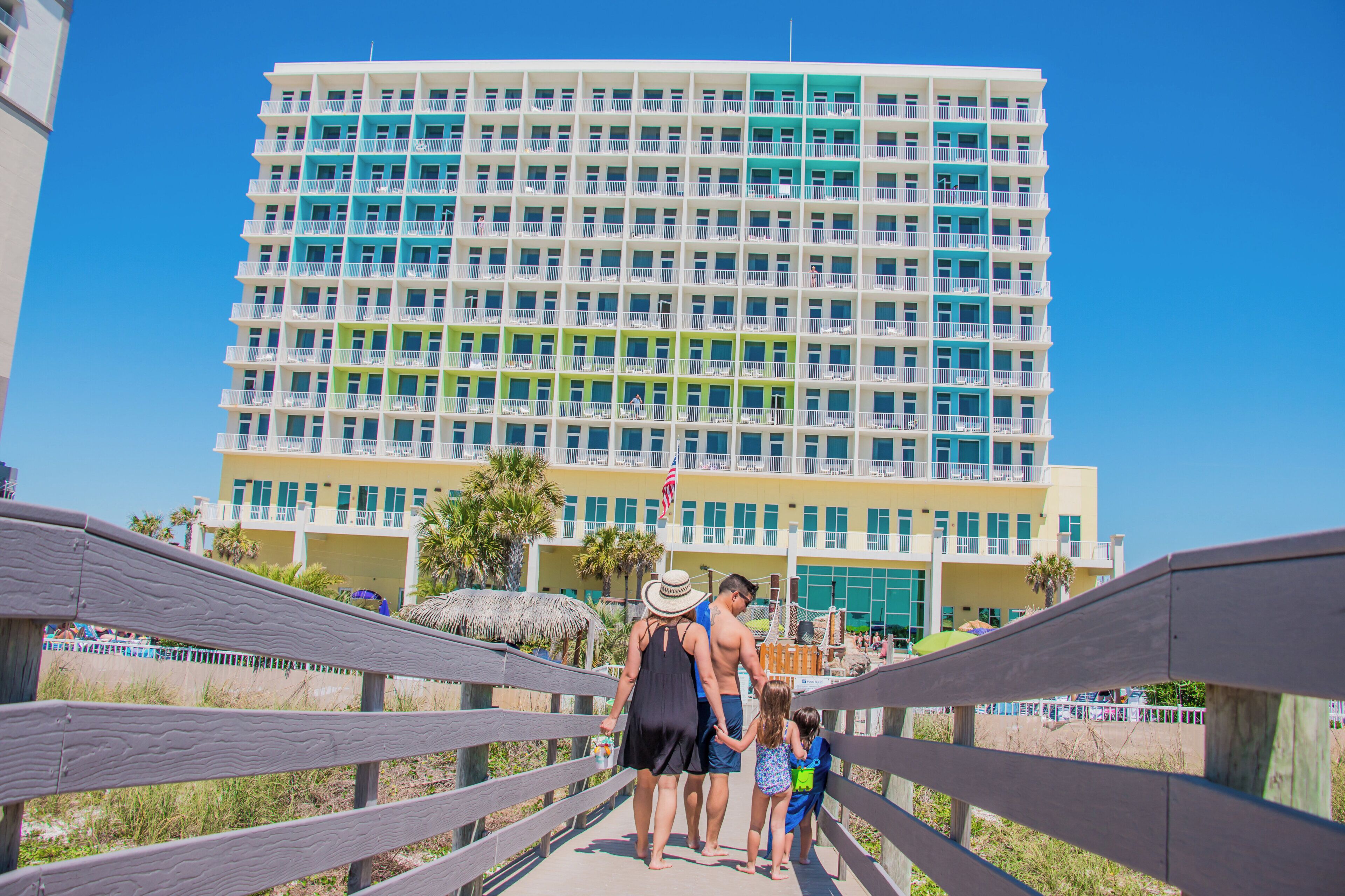 A multi-story hotel with balconies, a pool area, and a beach view.