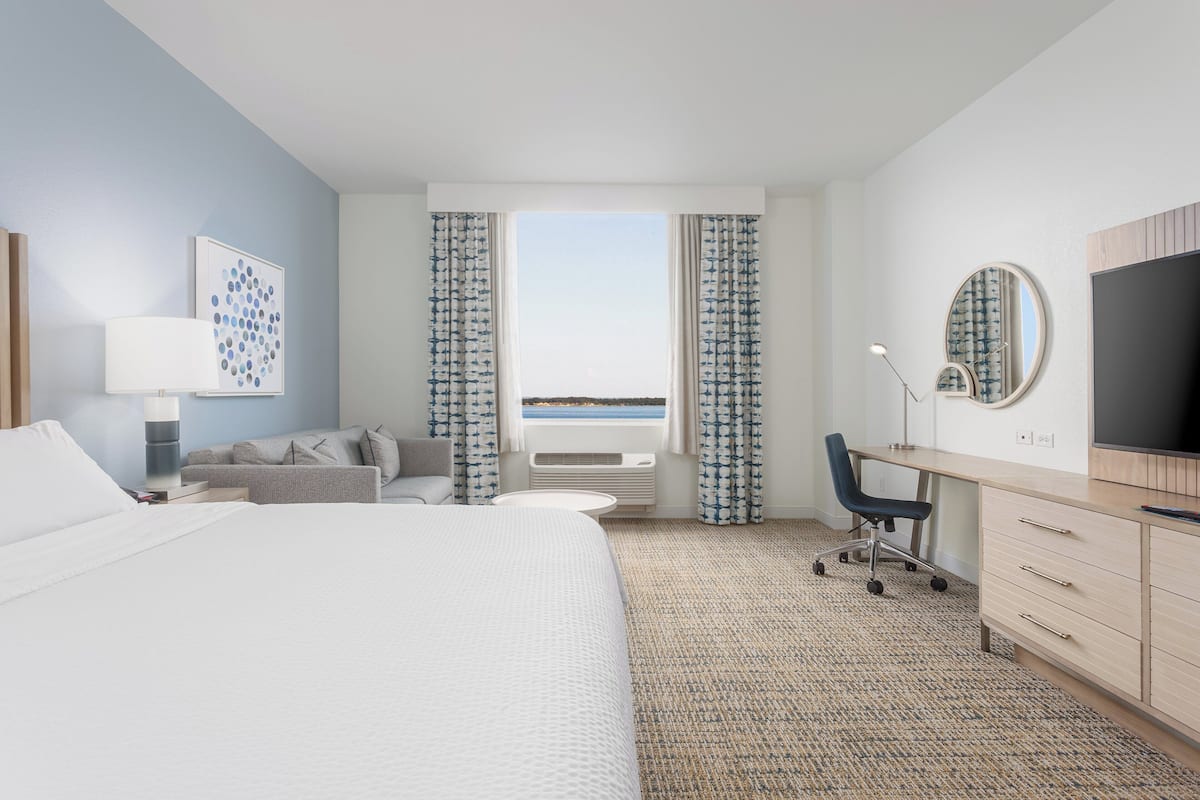 Ein Hotelzimmer mit Bett, Schreibtisch, Stuhl, Fernseher und Meerblick durch das Fenster.