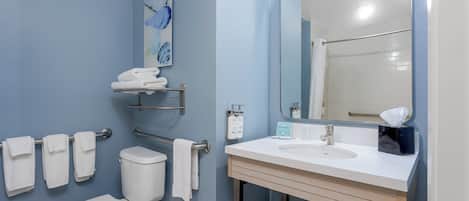 A bathroom with a white toilet, a sink with a mirror, and towels on a rack.