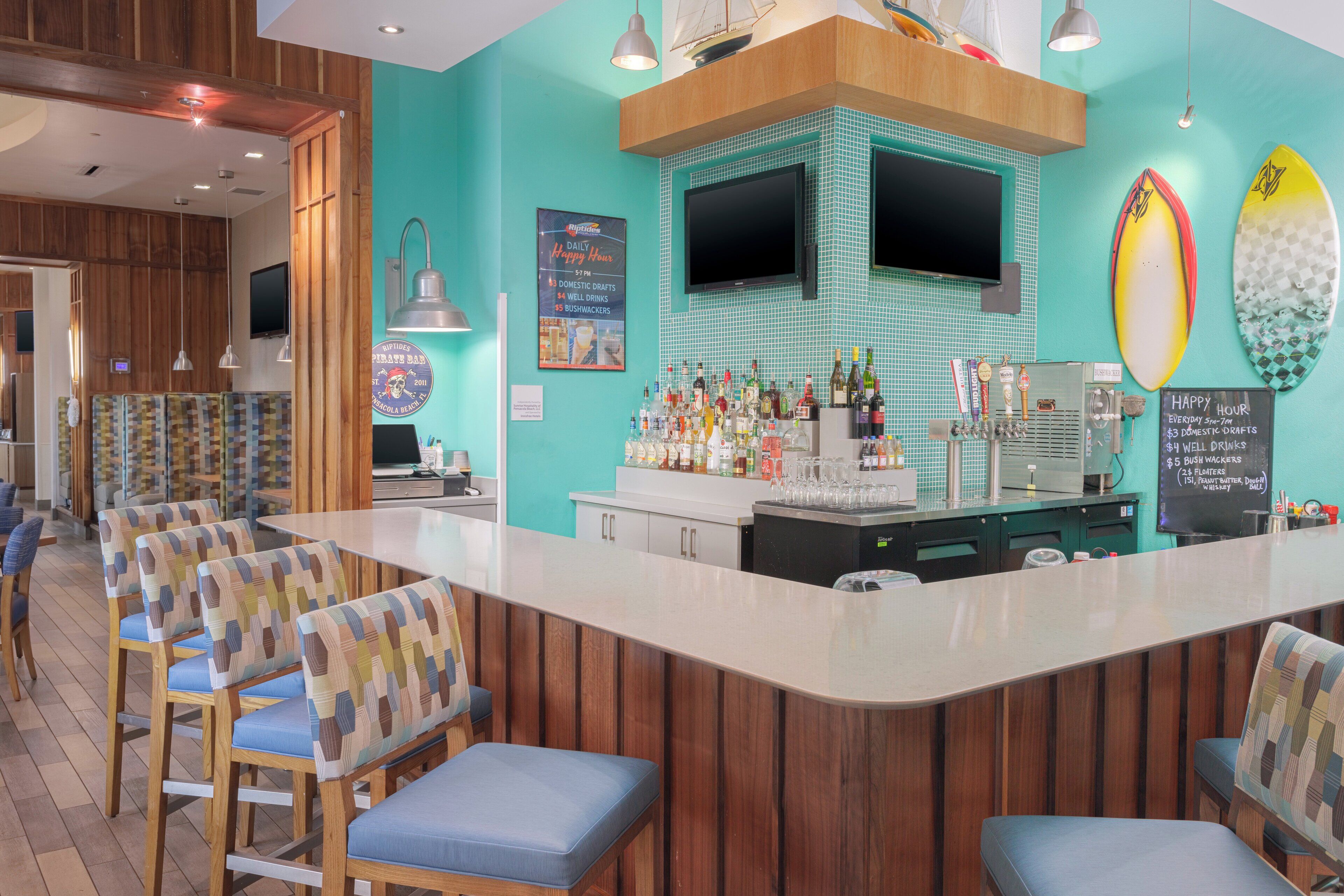 A bar area with wooden paneling, a counter with a variety of bottles, and surfboards on the wall.
