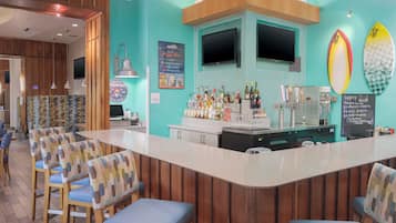 Zona de bar con paneles de madera, una barra con gran variedad de botellas y tablas de surf en la pared.