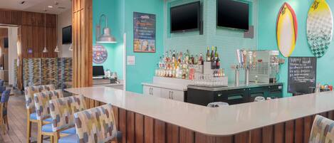 Zona de bar con paneles de madera, una barra con gran variedad de botellas y tablas de surf en la pared.