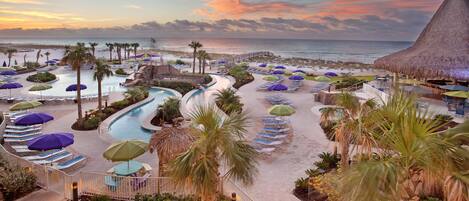 A resort with a swimming pool, lounge chairs, umbrellas, and a beach view.