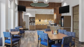 Un espace de salle à manger moderne avec des chaises à revêtement bleu et une table en bois, une cuisine en arrière-plan et un éclairage suspendu.