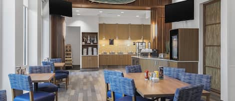Un espace de salle à manger moderne avec des chaises à revêtement bleu et une table en bois, une cuisine en arrière-plan et un éclairage suspendu.