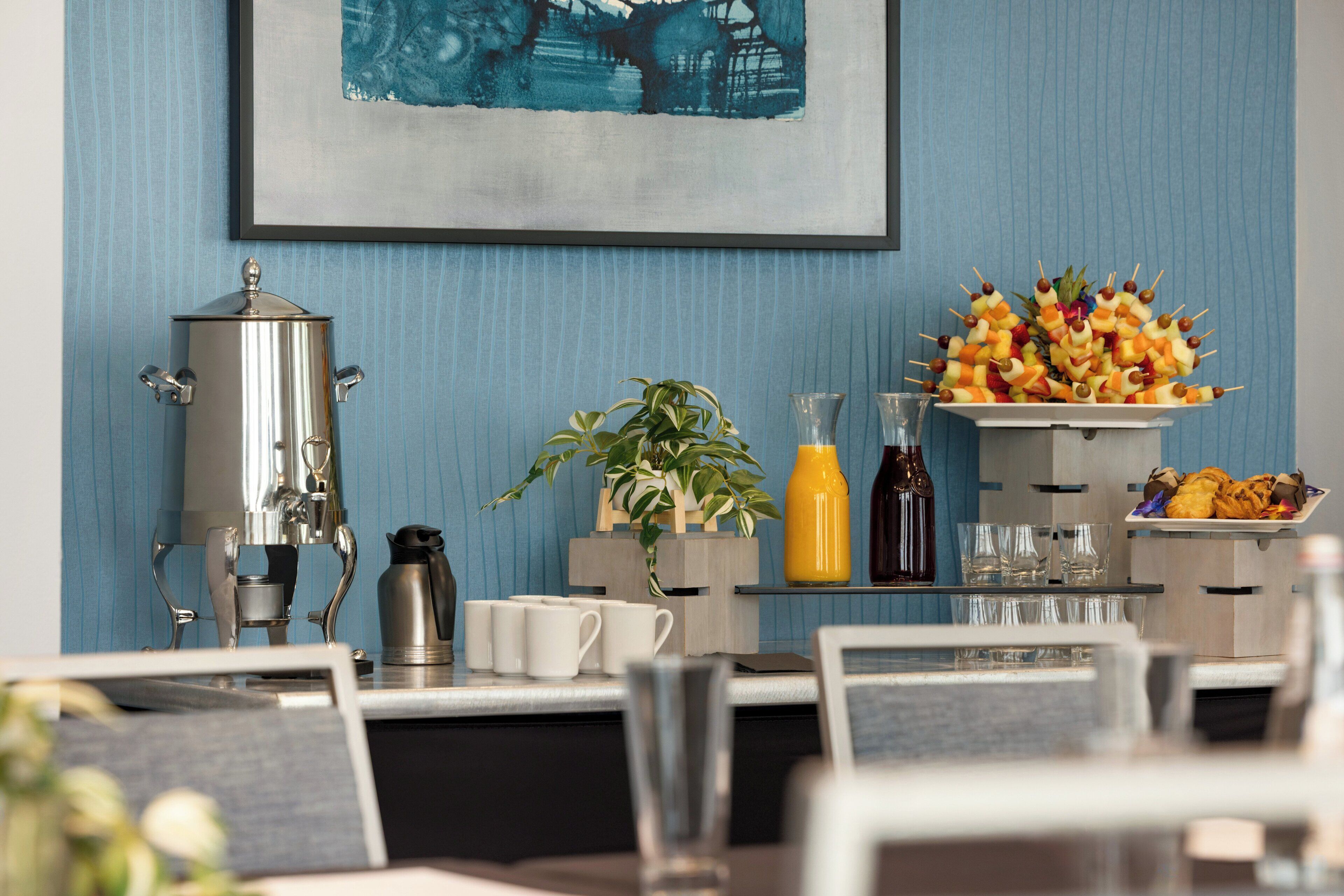 A breakfast buffet with a coffee maker, fruit skewers, and a plant.