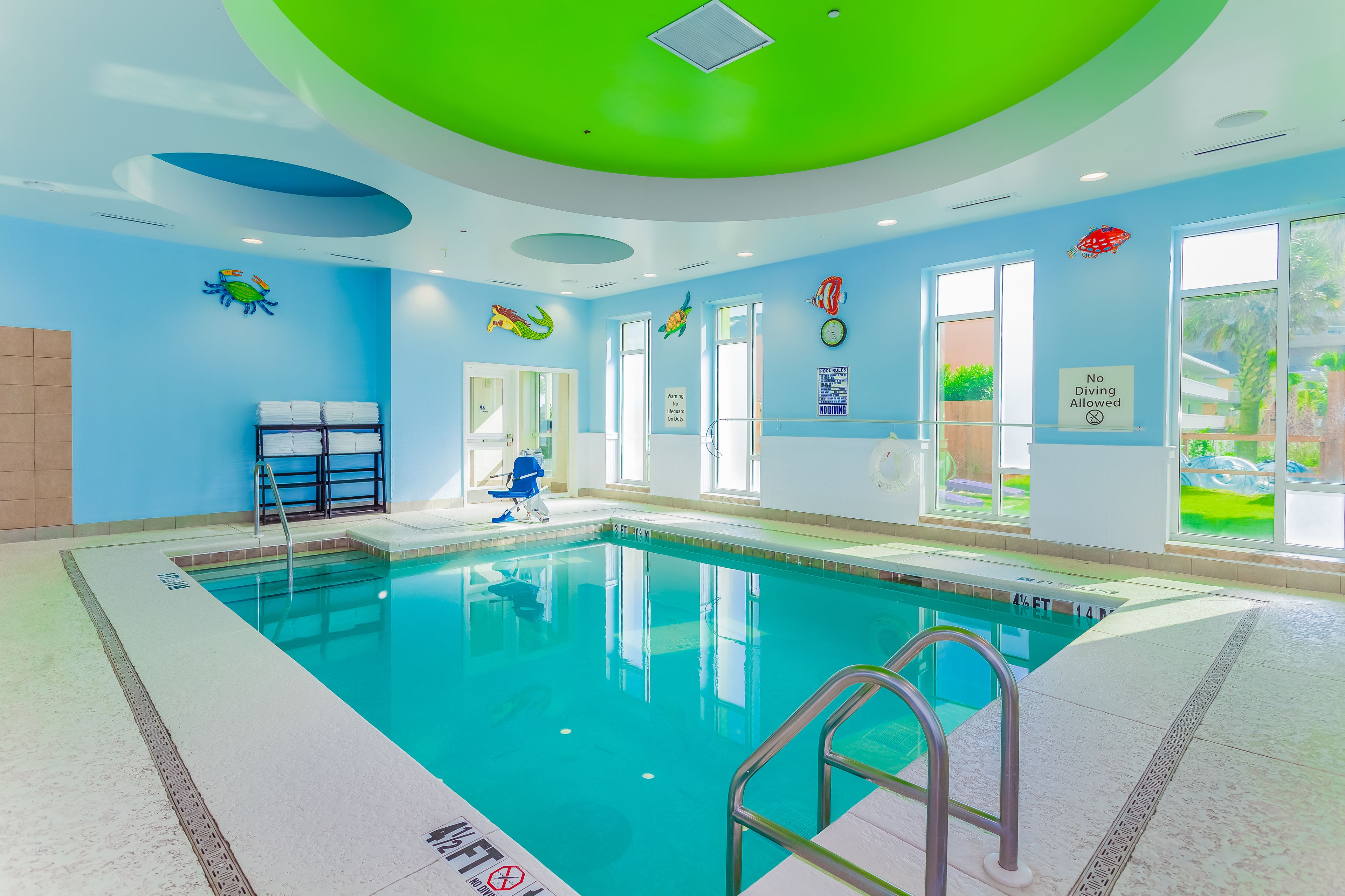 A swimming pool with clear water, surrounded by blue walls and green ceiling accents.