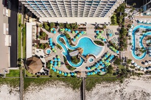 An aerial view of a resort with a central pool, multiple lounge areas, and a high-rise hotel in the background. - Holiday Inn Resort Pensacola Beach by IHG (Pensacola Beach)