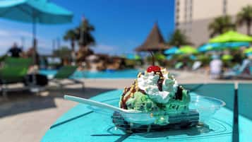 Un dessert su un piatto di plastica trasparente, guarnito con una ciliegina, posizionato su un tavolo color turchese in prossimità di una piscina.