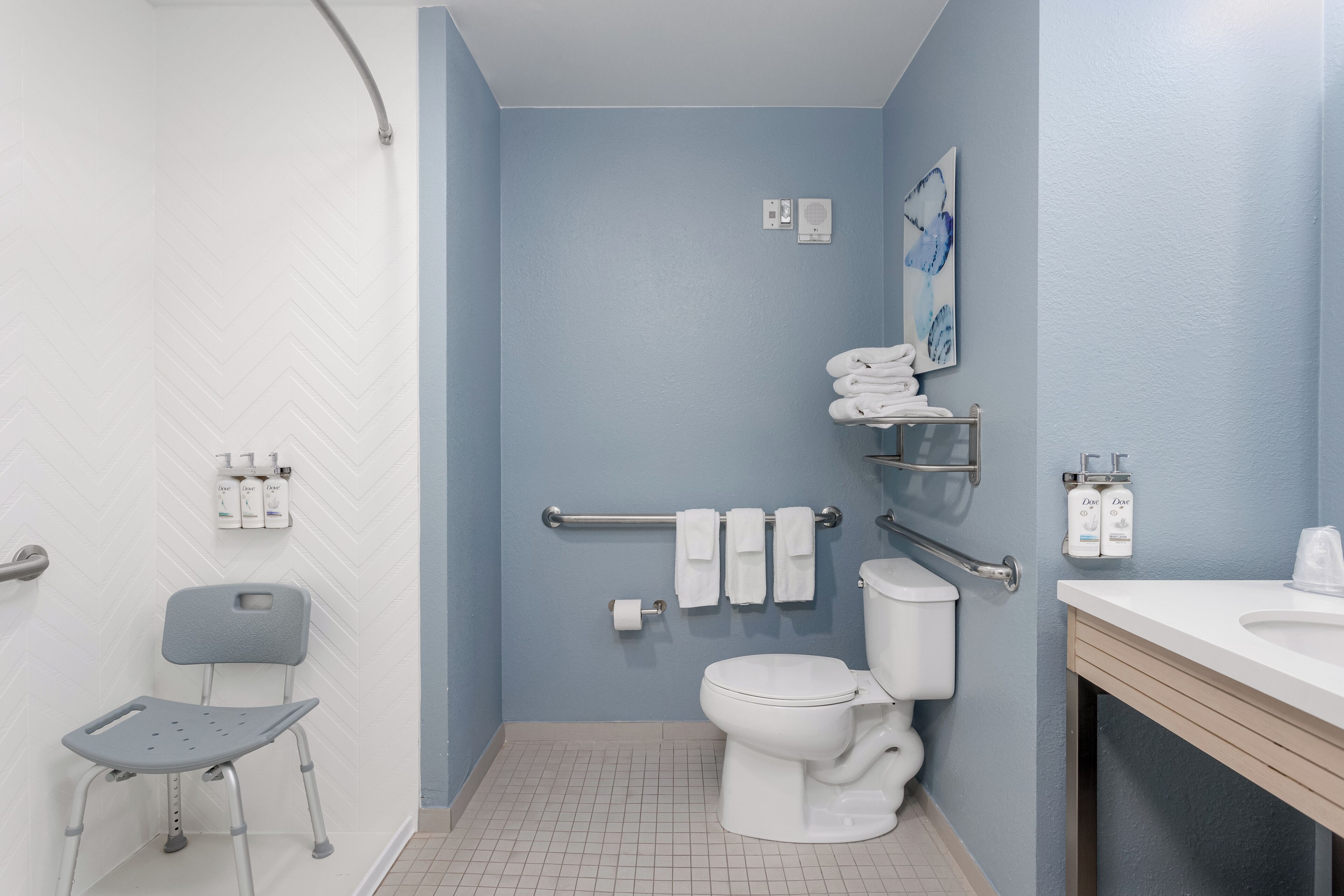 Un baño con inodoro blanco, silla de ducha y lavamanos.