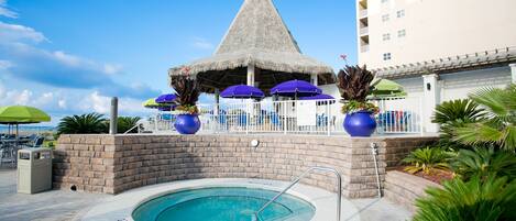 A swimming pool with a thatched-roof structure, surrounded by lounge chairs and umbrellas.