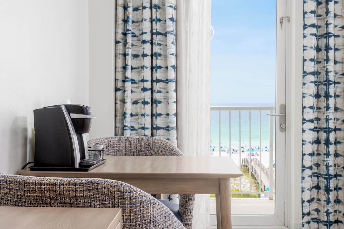 Ein Zimmer mit einer Kaffeemaschine auf einem Tisch, gemusterten Vorhängen und Blick auf den Strand.