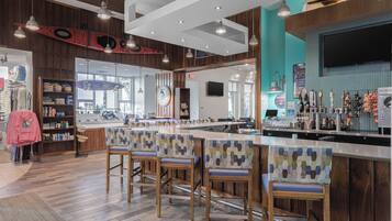 Zona de bar moderna con suelo de madera, taburetes con estampado y una barra con diversos artículos.