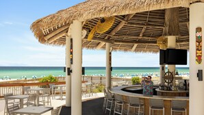 An outdoor bar area with a thatched roof, white chairs, and a view of the beach and ocean. - Holiday Inn Resort Pensacola Beach by IHG (Pensacola Beach)