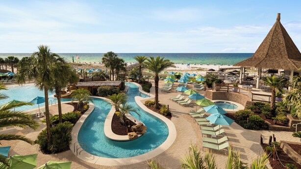 A resort pool area with a curved pool, lounge chairs, umbrellas, and a beach view. - Holiday Inn Resort Pensacola Beach by IHG (Pensacola Beach)