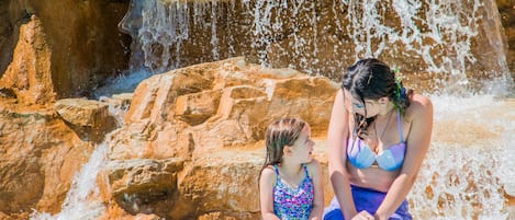 A woman and a child sitting on rocks near a waterfall.