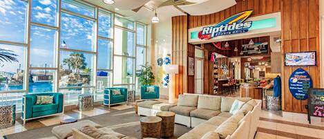 A spacious lobby with large windows, a Riptones Sports Grill, and comfortable seating areas.