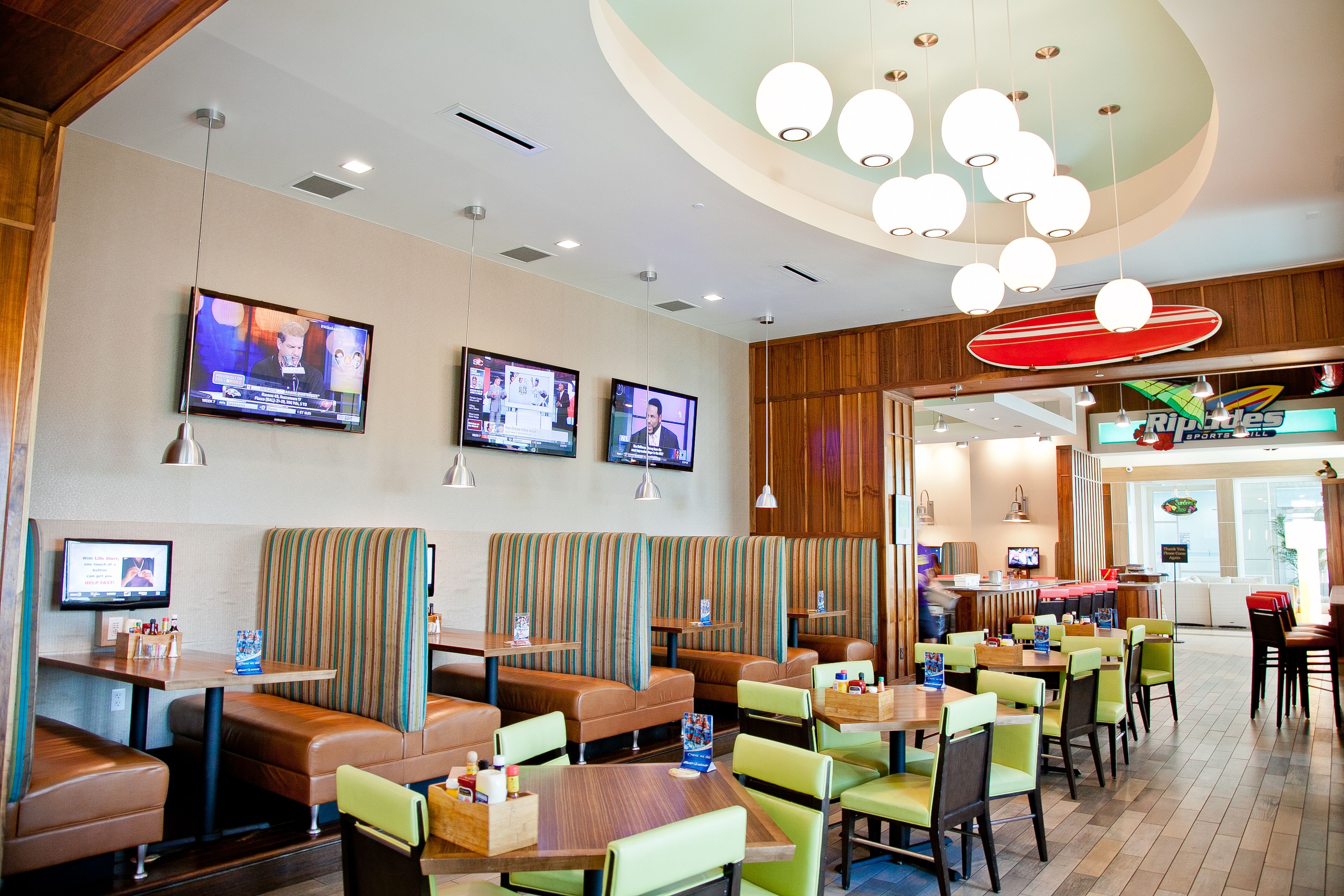 Un restaurante con cabinas y mesas, varios televisores en la pared y una decoración con una tabla de surf.