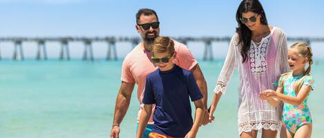 A family walking on a beach with a pier in the background.