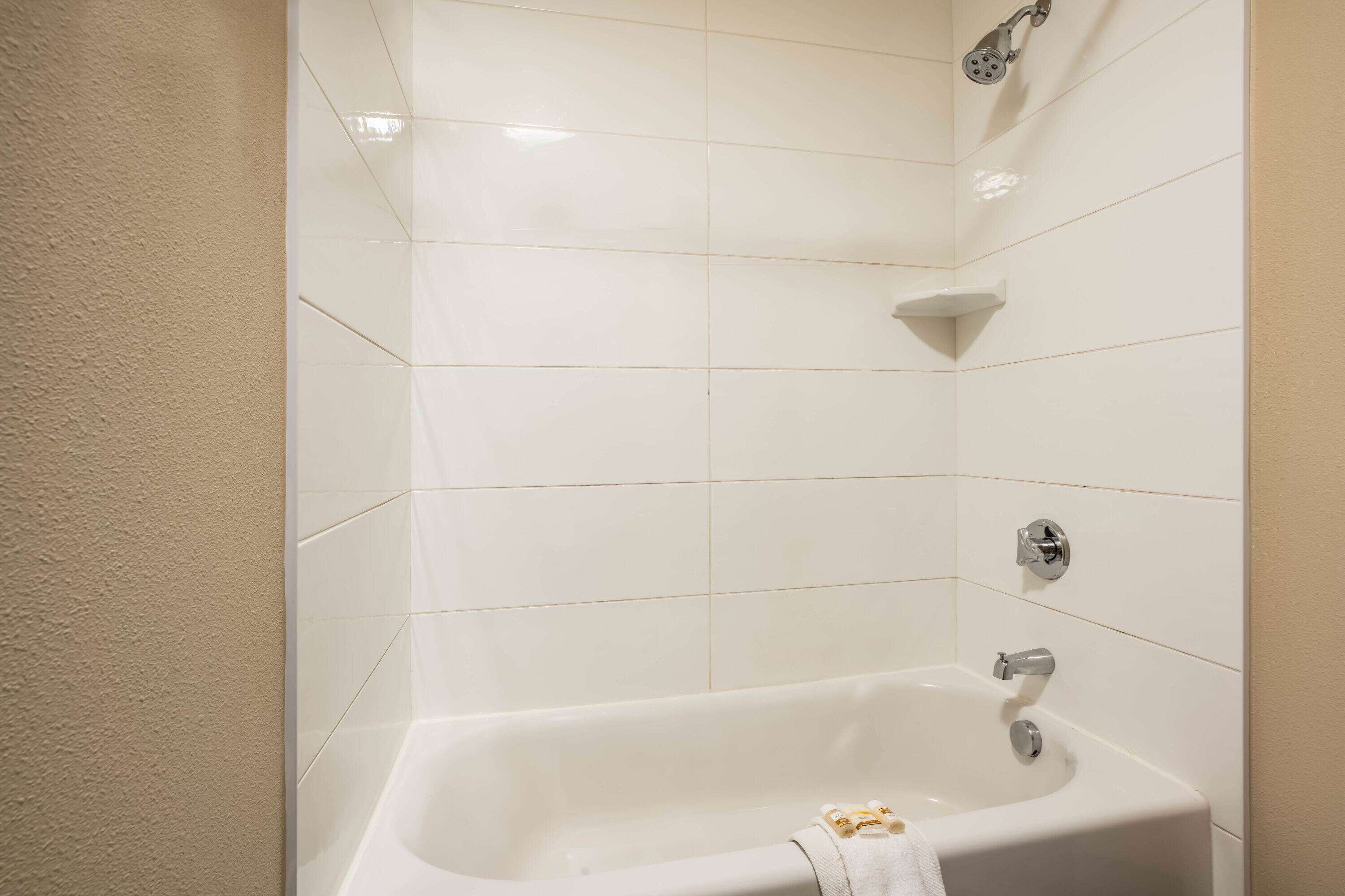 Une salle de bain avec des carreaux blancs, une baignoire, une pomme de douche et un porte-serviettes.