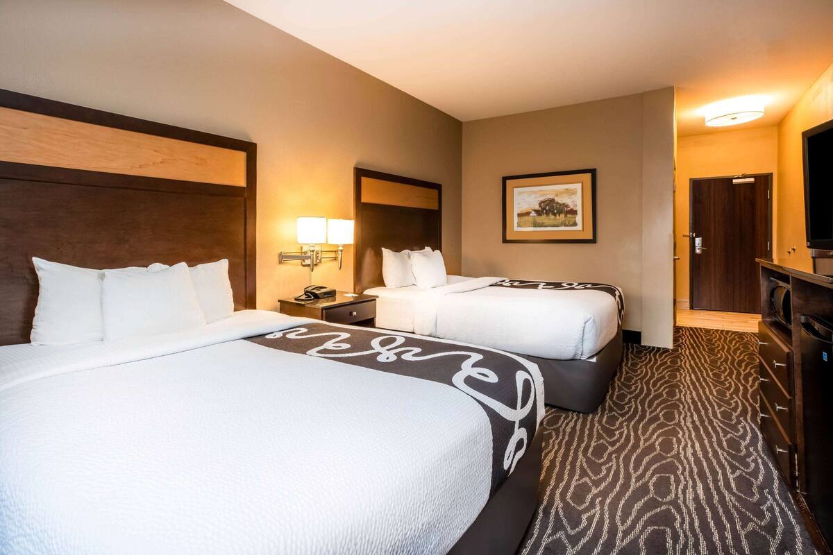 A hotel room with two beds, a nightstand, a lamp, a framed picture on the wall, and a television.