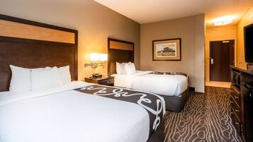 A hotel room with two beds, a nightstand, a lamp, a framed picture on the wall, and a television.