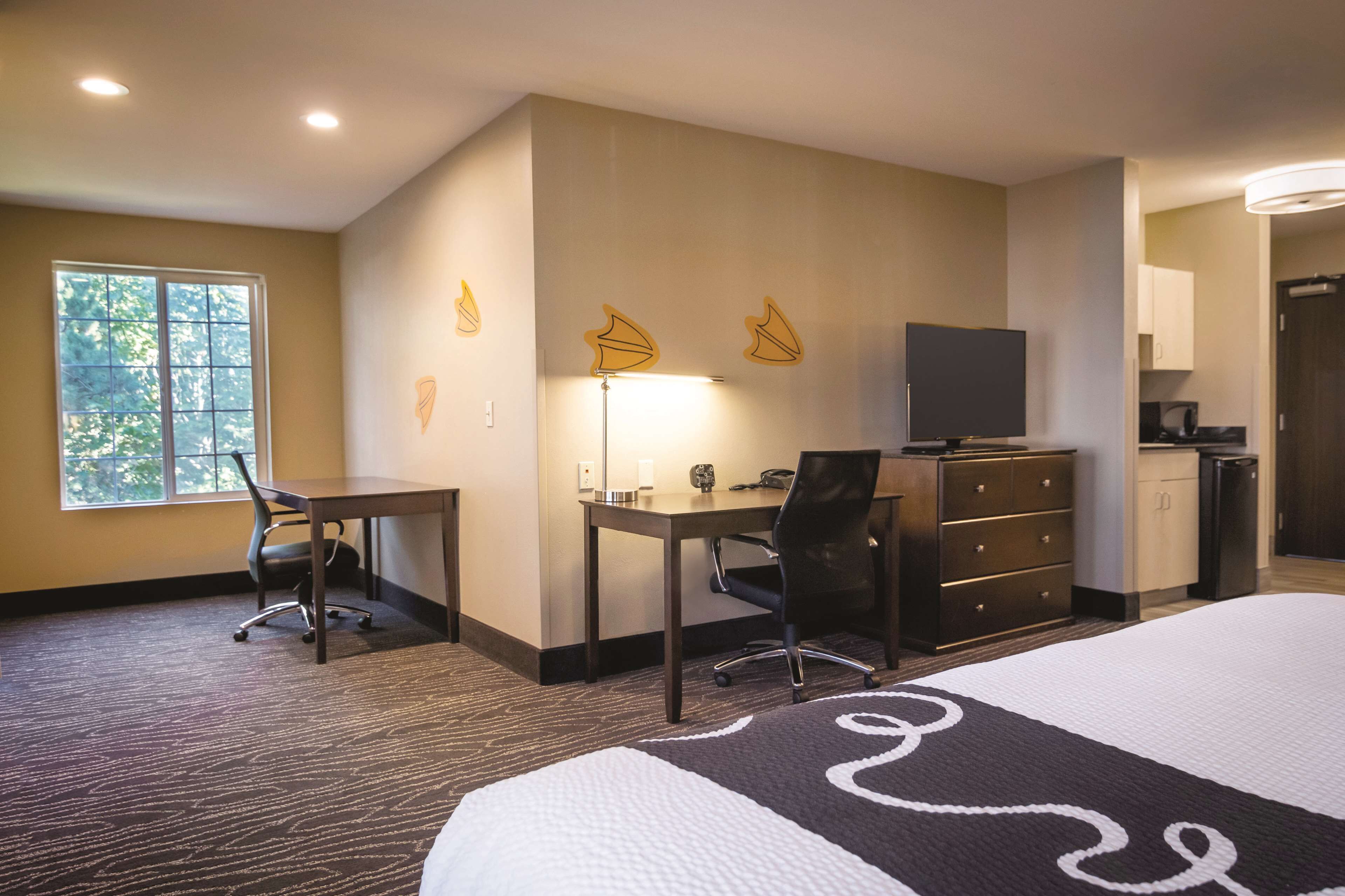 A hotel room with a bed, desk, chair, TV, and kitchenette.