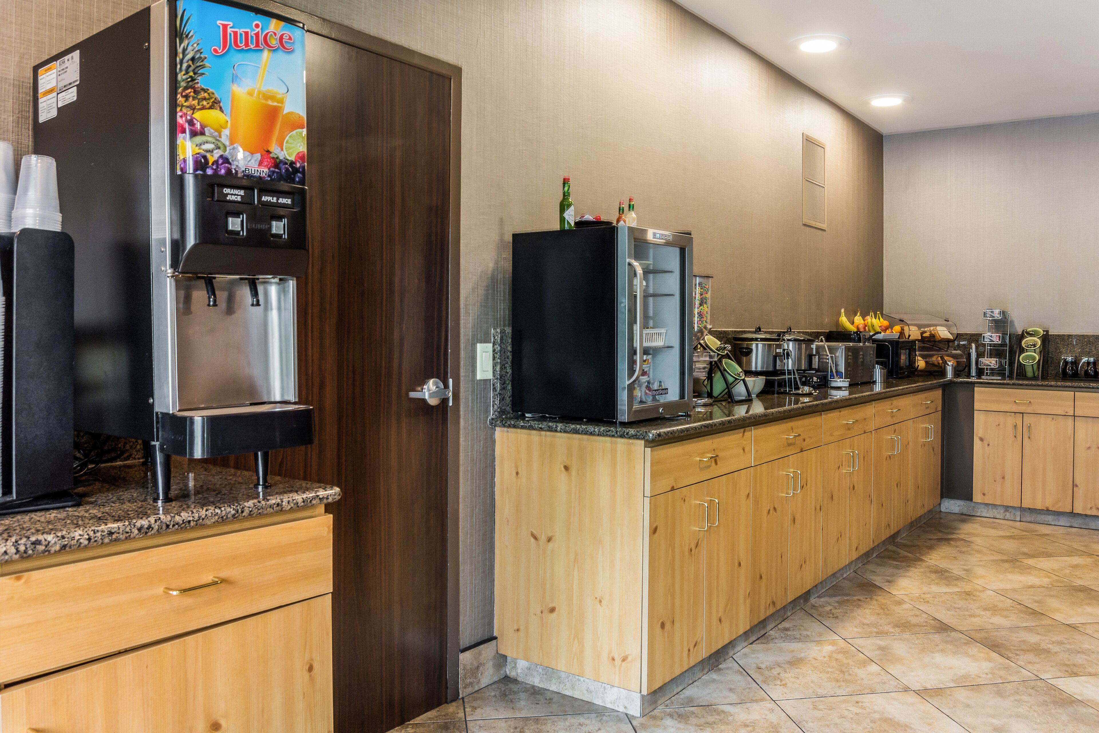 A kitchen with a juice dispenser, a refrigerator, and a microwave.