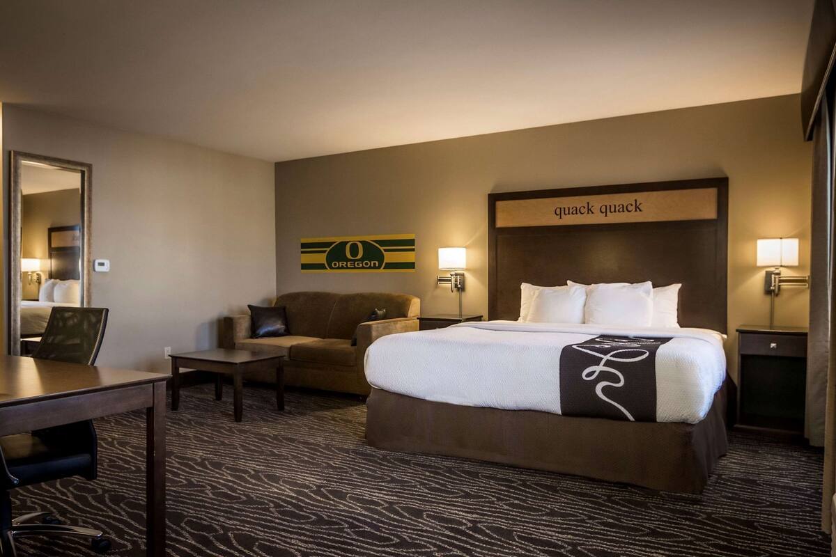 A hotel room with a bed, a sofa, a desk, and a mirror.