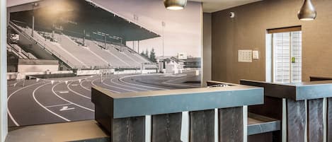 Zona de recepción con un mural de un estadio, mostrador e iluminación colgante.
