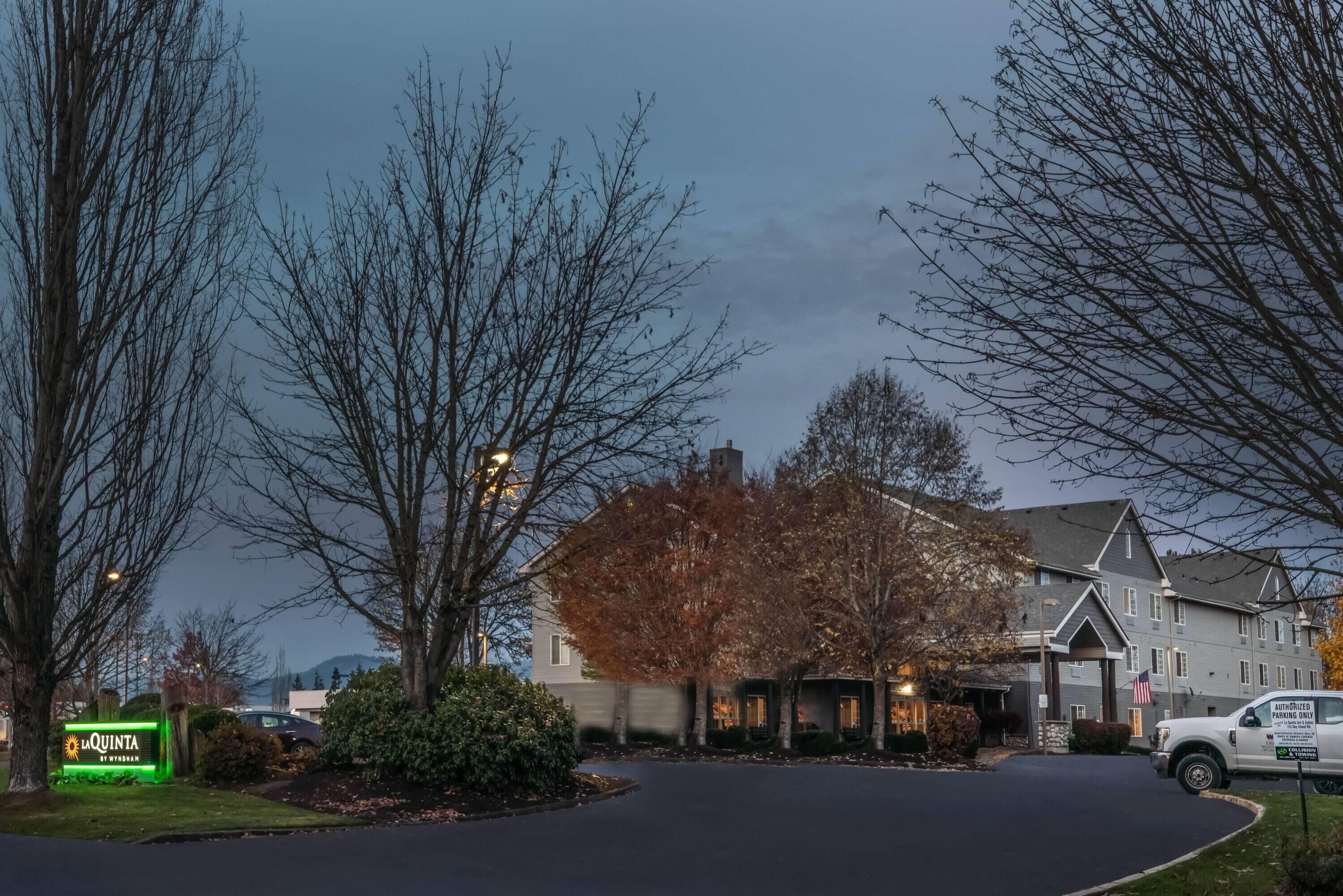 A hotel entrance with a sign, a driveway, and a building with a flag.