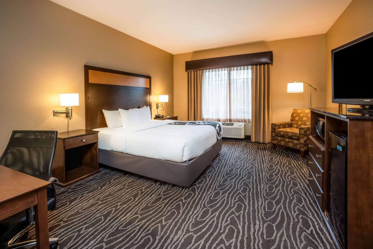 A hotel room with a large bed, a desk, a chair, a television, and a window with curtains.
