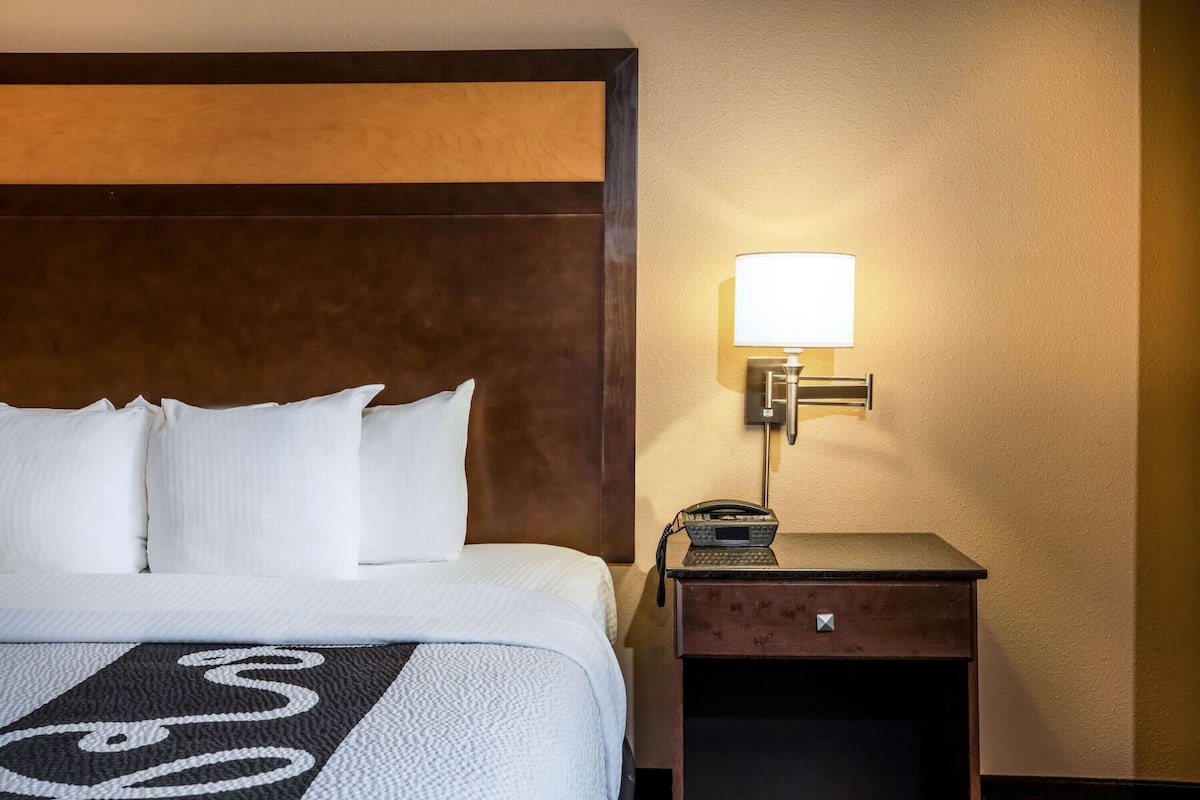 A hotel room with a large bed, white bedding, a headboard, a bedside table with a lamp, and a telephone.