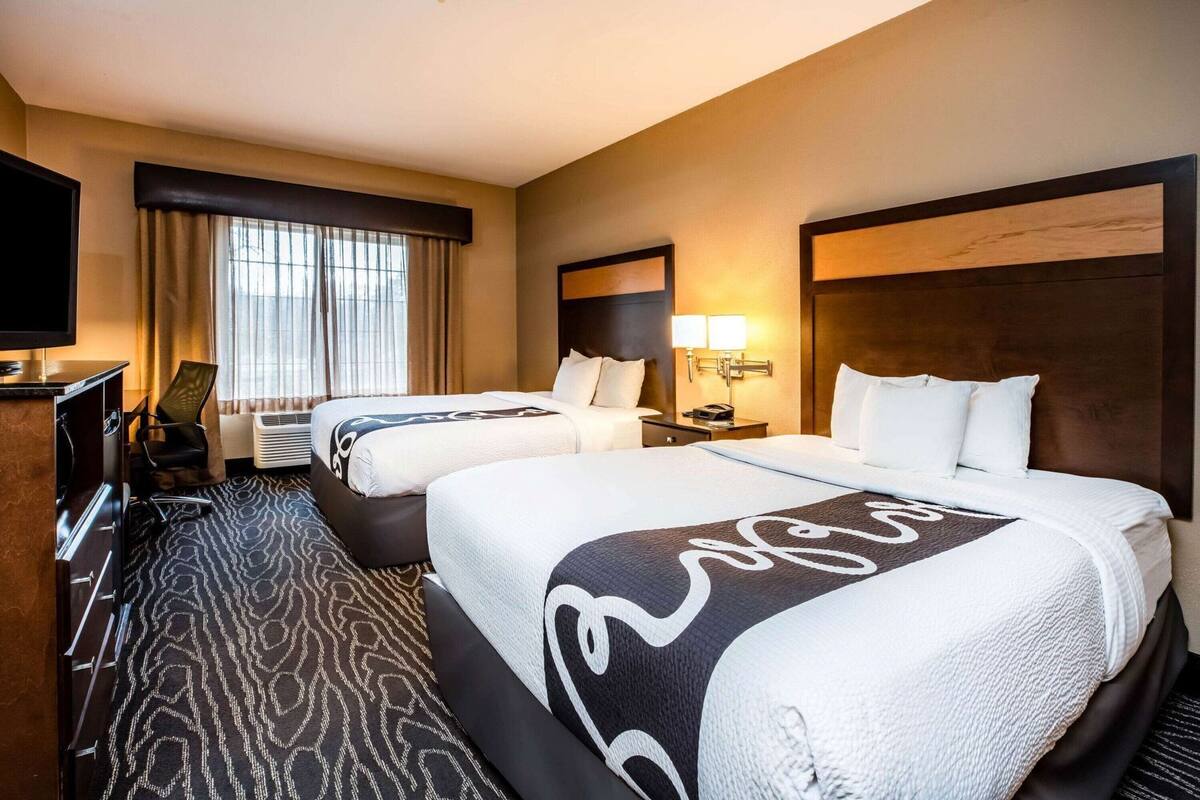 A hotel room with two beds, a TV, a desk, and a chair.