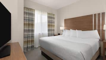 A hotel room with a large bed, a flat-screen TV, a wooden nightstand, and a window with curtains.