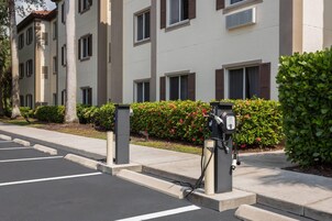 A parking area with electric vehicle charging stations, a sidewalk, and a building with multiple windows and shutters.